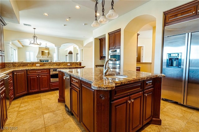 kitchen with sink, light stone counters, decorative light fixtures, appliances with stainless steel finishes, and a kitchen island with sink