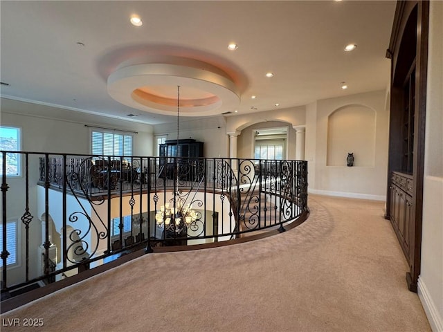 hall featuring light colored carpet, decorative columns, and a raised ceiling