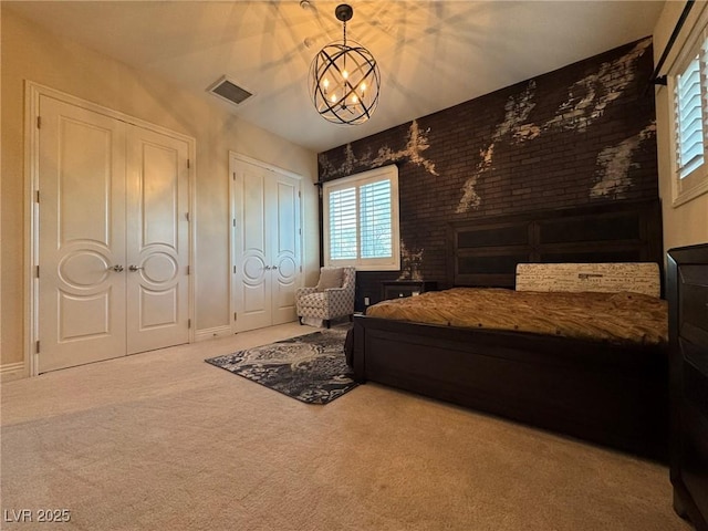 carpeted bedroom with multiple closets, brick wall, and a chandelier