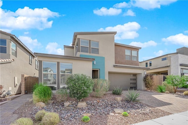 view of front facade featuring decorative driveway, fence, an attached garage, and stucco siding