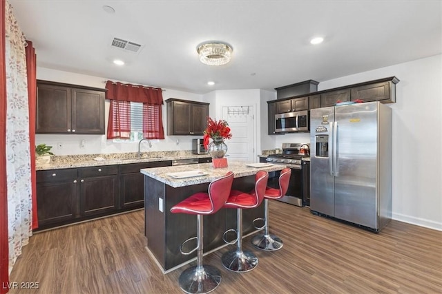 kitchen featuring sink, dark wood-type flooring, appliances with stainless steel finishes, a center island, and light stone countertops