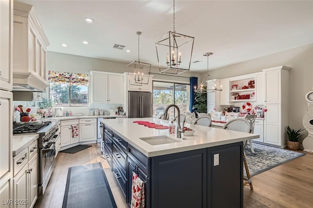 kitchen with decorative light fixtures, sink, white cabinets, high end appliances, and a kitchen island with sink