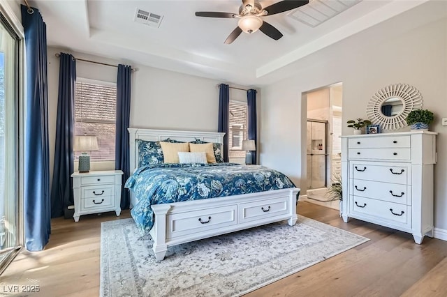 bedroom featuring ensuite bathroom, a raised ceiling, and light wood-type flooring