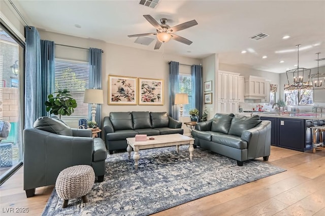 living room featuring ceiling fan with notable chandelier and light hardwood / wood-style floors