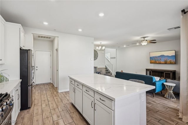 kitchen with white cabinetry, light stone counters, a center island, appliances with stainless steel finishes, and ceiling fan with notable chandelier