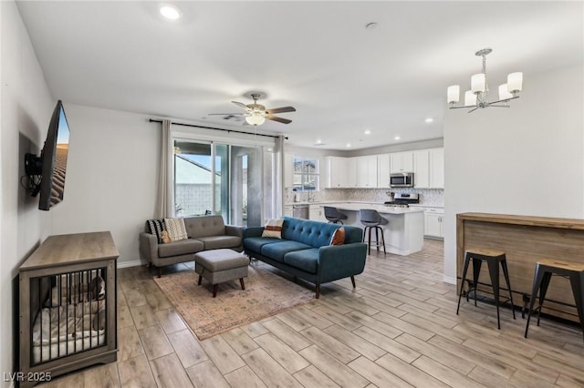 living room with ceiling fan with notable chandelier and light hardwood / wood-style flooring