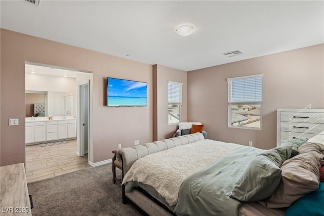 bedroom featuring connected bathroom and light hardwood / wood-style flooring