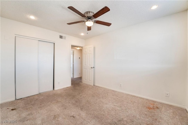 unfurnished bedroom with ceiling fan, light colored carpet, a closet, and a textured ceiling