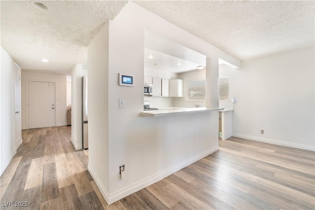 hallway featuring kitchen peninsula, light wood-type flooring, a textured ceiling, and white cabinets