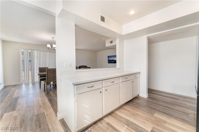 kitchen with white cabinetry, a chandelier, a textured ceiling, and light hardwood / wood-style flooring