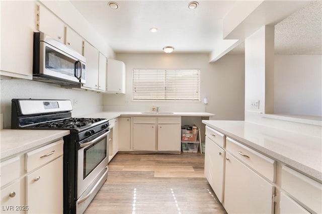 kitchen featuring stainless steel appliances, sink, white cabinets, and light wood-type flooring