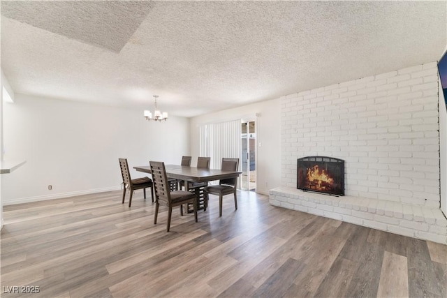 dining area with a fireplace, a textured ceiling, wood-type flooring, and a chandelier