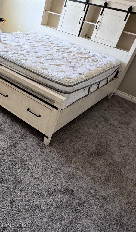 unfurnished bedroom featuring a barn door and dark carpet