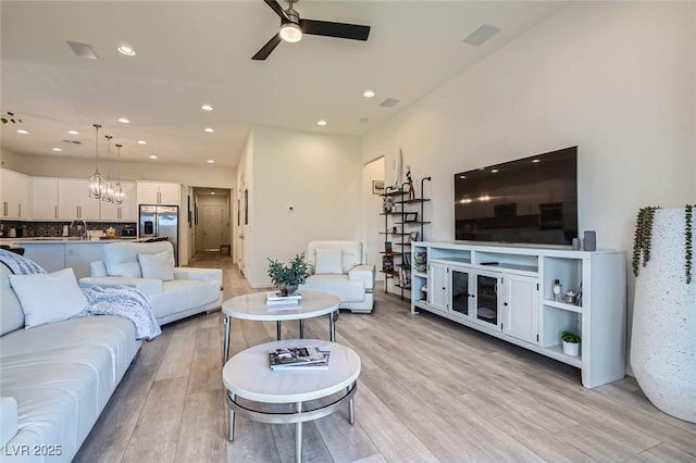 living room with sink, ceiling fan with notable chandelier, and light hardwood / wood-style floors