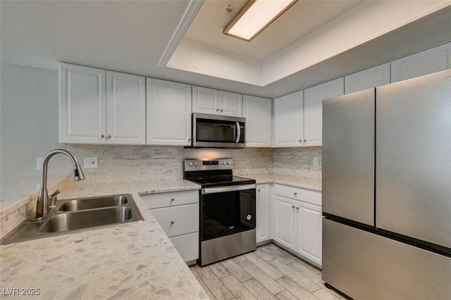 kitchen with sink, appliances with stainless steel finishes, a raised ceiling, decorative backsplash, and white cabinets