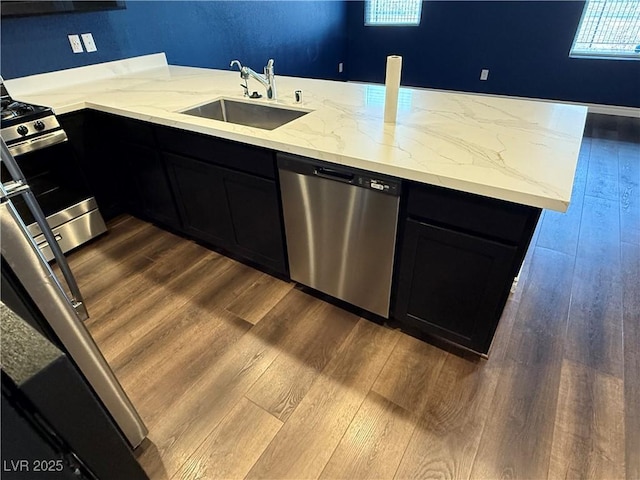 kitchen with sink, dark wood-type flooring, stainless steel appliances, light stone counters, and kitchen peninsula