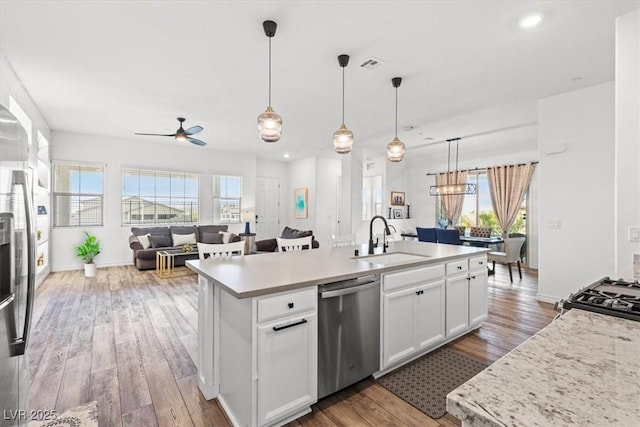 kitchen with sink, hanging light fixtures, appliances with stainless steel finishes, a kitchen island with sink, and white cabinets