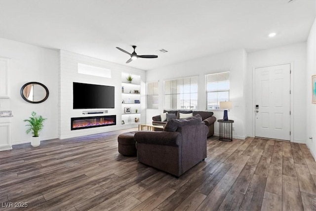 living room featuring dark hardwood / wood-style flooring, built in features, a large fireplace, and ceiling fan