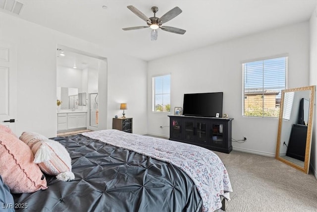 bedroom with multiple windows, ensuite bathroom, light colored carpet, and ceiling fan