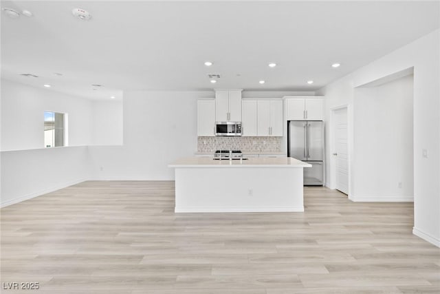 kitchen featuring white cabinets, decorative backsplash, stainless steel appliances, a center island with sink, and light hardwood / wood-style flooring