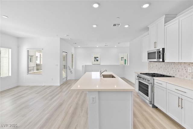 kitchen with appliances with stainless steel finishes, sink, a center island with sink, and white cabinets