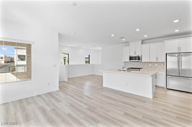 kitchen featuring sink, white cabinetry, appliances with stainless steel finishes, a kitchen island with sink, and decorative backsplash