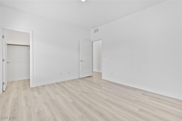 unfurnished bedroom with a spacious closet, a closet, and light wood-type flooring