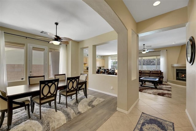 dining space with light tile patterned floors, a large fireplace, and ceiling fan