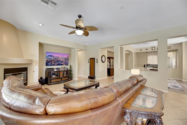 living room featuring a large fireplace, light tile patterned floors, and ceiling fan