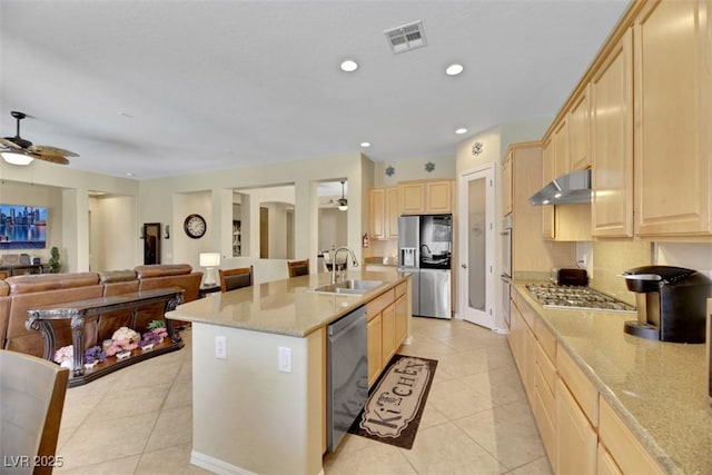 kitchen featuring stainless steel appliances, light brown cabinetry, sink, and a center island with sink