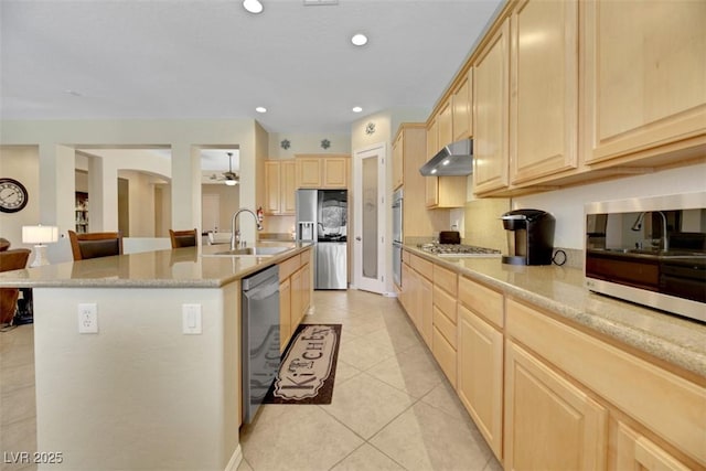 kitchen featuring sink, light tile patterned floors, light brown cabinets, appliances with stainless steel finishes, and an island with sink