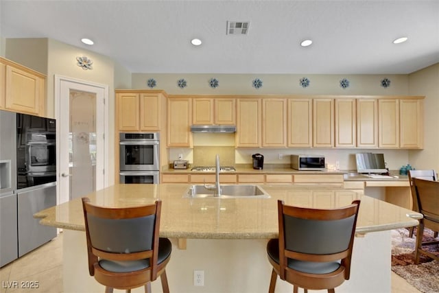 kitchen with a kitchen bar, sink, a center island with sink, light brown cabinets, and stainless steel appliances