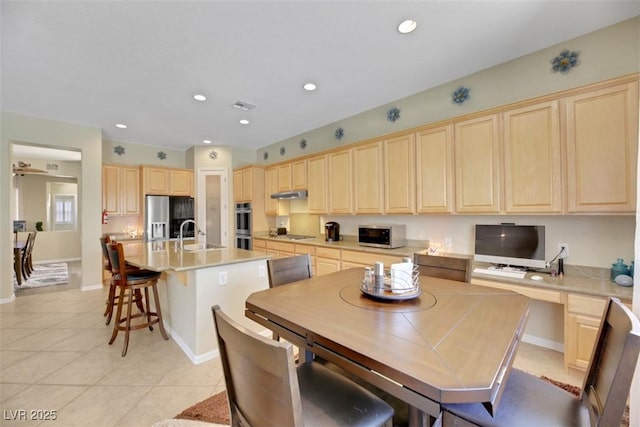 kitchen with a kitchen island with sink, light brown cabinetry, built in desk, and stainless steel appliances