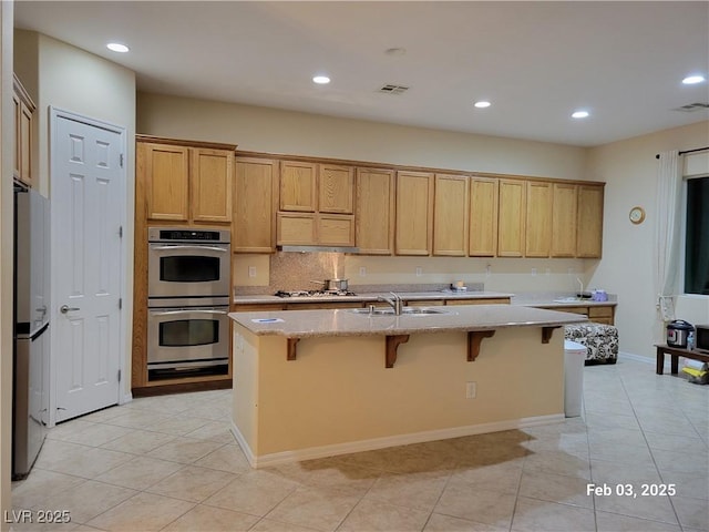 kitchen featuring a center island with sink, a kitchen bar, sink, light stone counters, and stainless steel appliances