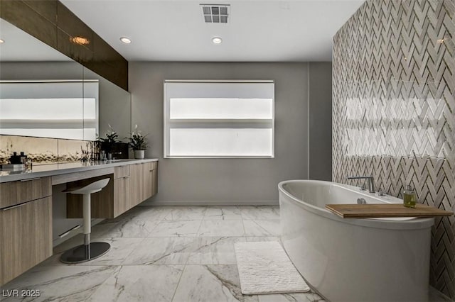 full bath featuring visible vents, marble finish floor, vanity, a freestanding tub, and recessed lighting