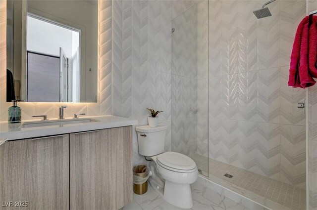 bathroom featuring marble finish floor, tile walls, toilet, a tile shower, and vanity