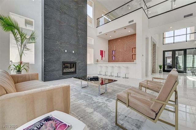 living room featuring marble finish floor, visible vents, a high ceiling, and a premium fireplace