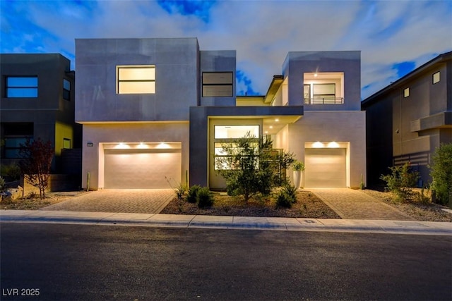 contemporary house with decorative driveway, an attached garage, and stucco siding