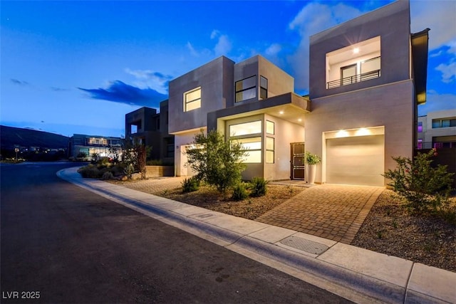 view of front of house featuring decorative driveway, an attached garage, and stucco siding