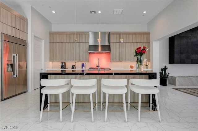 kitchen featuring stainless steel built in fridge, modern cabinets, pendant lighting, and wall chimney range hood