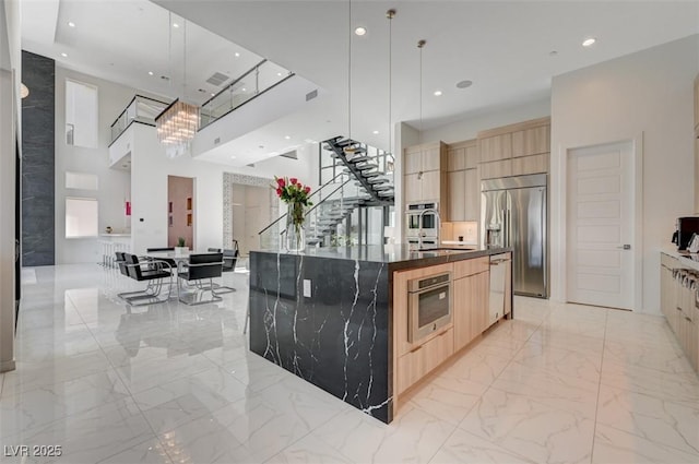 kitchen with marble finish floor, hanging light fixtures, light brown cabinetry, an island with sink, and stainless steel built in refrigerator