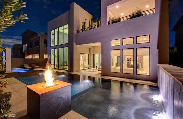 back of property featuring a patio area, a fire pit, stucco siding, and an in ground hot tub