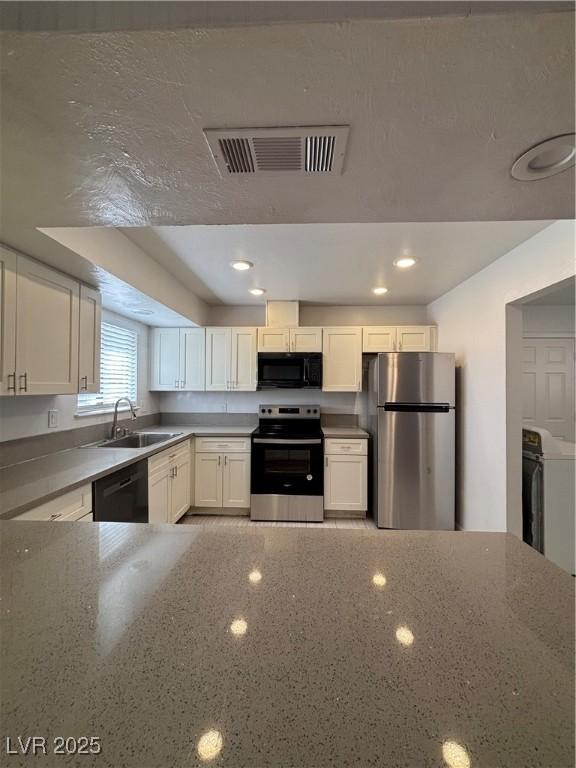 kitchen featuring white cabinetry, washer / dryer, sink, and black appliances