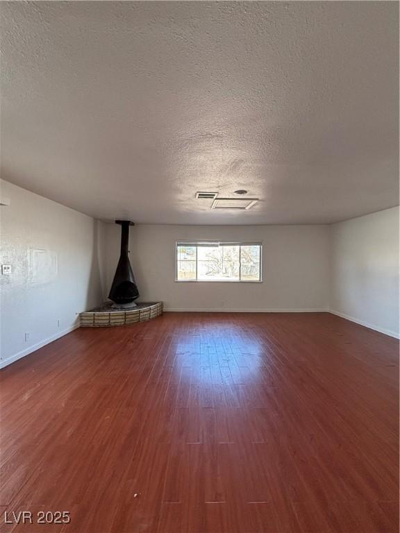 unfurnished living room featuring hardwood / wood-style flooring, a wood stove, and a textured ceiling