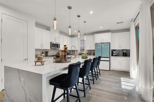 kitchen with decorative light fixtures, tasteful backsplash, white cabinetry, fridge, and light stone countertops