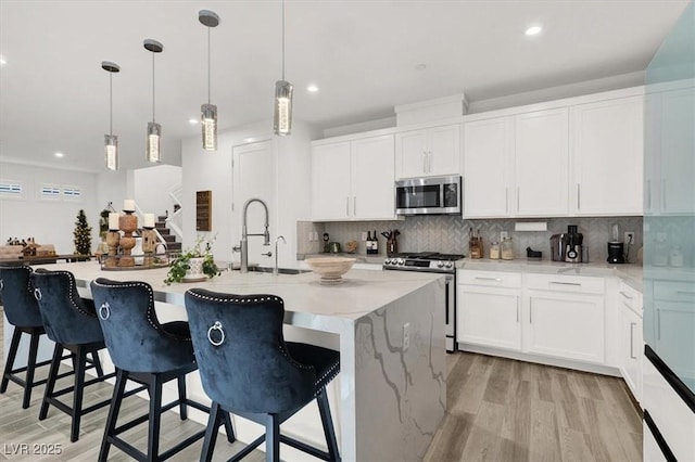 kitchen with a breakfast bar, white cabinetry, hanging light fixtures, stainless steel appliances, and a center island with sink