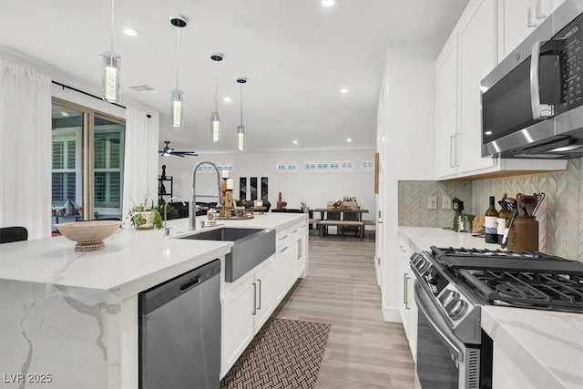 kitchen with decorative light fixtures, sink, stainless steel appliances, light stone countertops, and a center island with sink