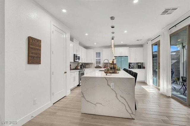 kitchen with white cabinetry, hanging light fixtures, appliances with stainless steel finishes, a kitchen island with sink, and light hardwood / wood-style floors