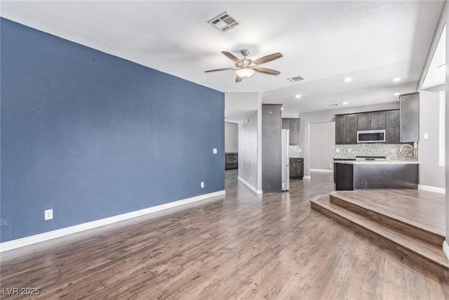 unfurnished living room featuring dark wood-type flooring, sink, and ceiling fan