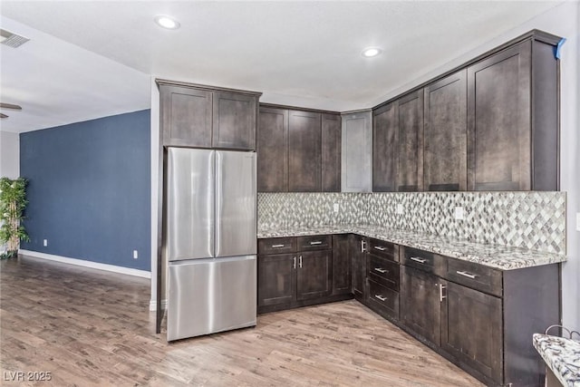 kitchen with light stone counters, dark brown cabinets, stainless steel refrigerator, and light hardwood / wood-style flooring